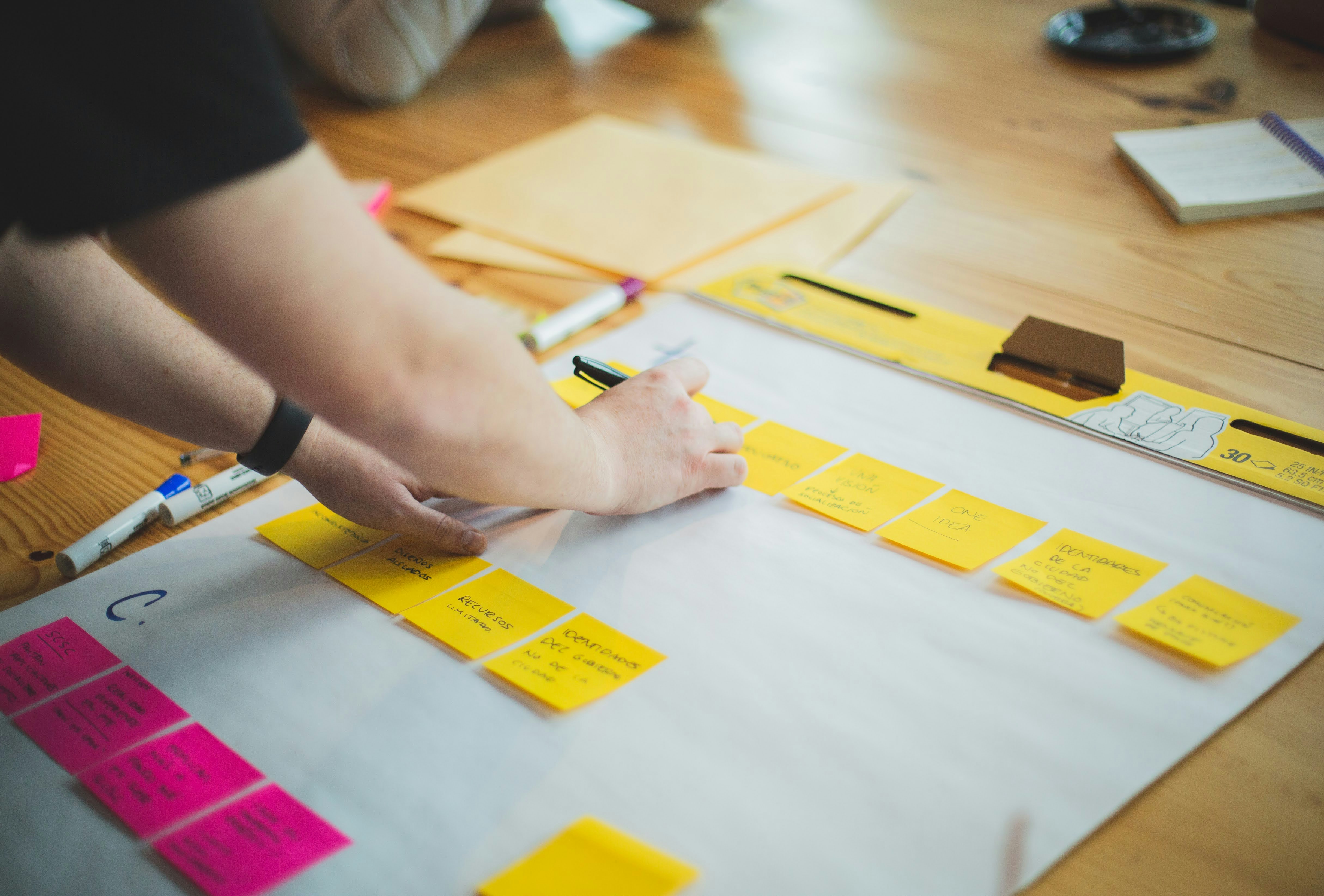 Hands arranging sticky notes across a paper framework on a table during a co-design session